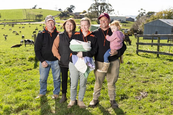 A Family Posing In Front Of A Farm With Cows.